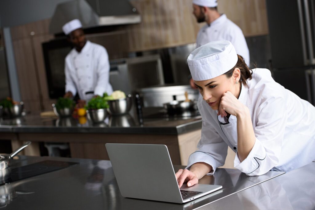 Attractive,Chef,Using,Laptop,At,Restaurant,Kitchen